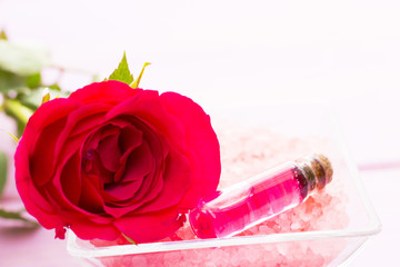 Spa and wellness setting with rose flower, sea salt, oil in a bottle on wooden white background