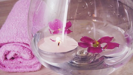Romantic composition with a candle and violet flowers floating in a bowl of water.The concept of Spa,cosmetic,procedure,treatment.