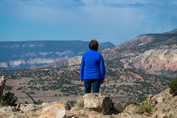 Woman wearing a blue fleece pullover looking out over a vast colorful landscape and stormy clouds in the American Southwest