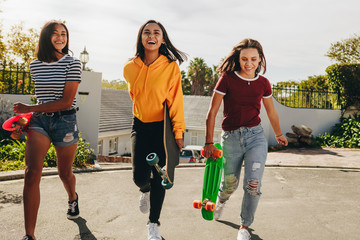 Teenage girls walking on street holding skateboards