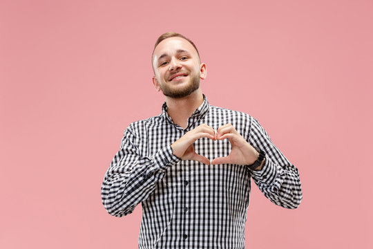 I love you. Portrait of attractive man showing the heart with fingers. pink studio. Beautiful male portrait. Young happy emotional funny man looking at camera. Human facial emotions concept. Trendy