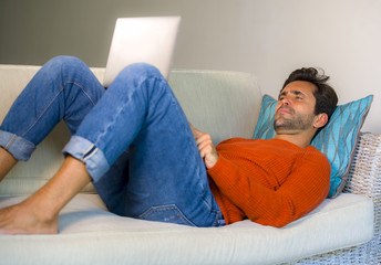 young happy and attractive man working relaxed with laptop computer at modern apartment living room sitting at sofa couch typing and networking confident and positive