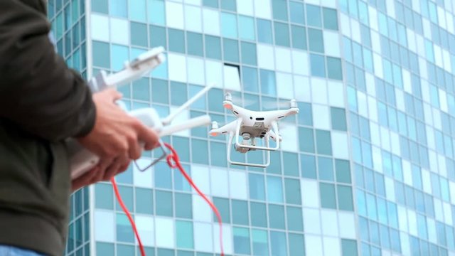 Young man flying quadro drone with modern white RC transmitter. Male filmer controlling drone over RC radio controller. Man filming with drone camera near industrial city and high-tech building