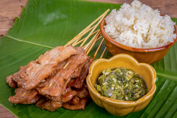 grilled pork or moo ping in Thai with sticky rice and Nam Prik Num (Northern Thai Green Chilli Dip) local street food on banana green leaf