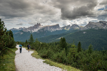 Fototapeta na wymiar climbers walking down a road in a Dolomite mountain landscape after a hard climb with a great panorama view behind them of the Alta Badia mountains