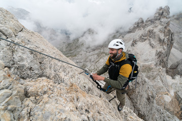 young male climber on a steep and exposed rock face climbing a Via Ferrata