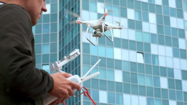 Young man flying quadro drone with modern white RC transmitter. Male filmer controlling drone over RC radio controller. Man filming with drone camera near industrial city and high-tech building