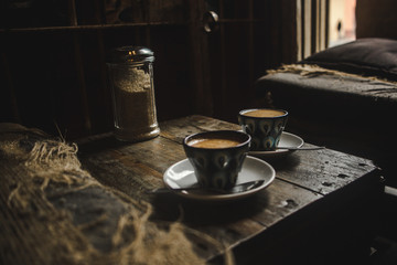 Two cortado coffees in hand-painted coffee cups on a wooden table in a cozy rustic café
