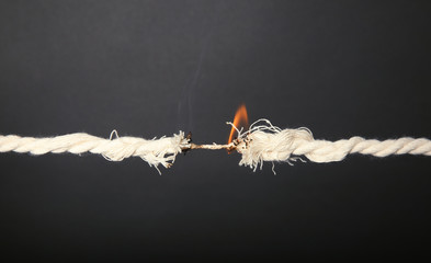 Burning frayed rope at breaking point on gray background