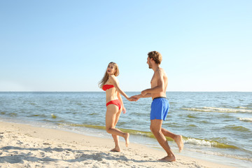 Happy young couple in beachwear running together on seashore