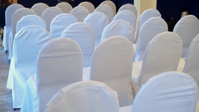 Chair with white cover cloth back side in a row in a big hall for wedding, conference or seminar steadicam