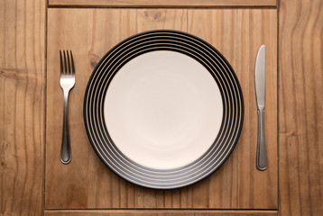 Empty plate with fork and knife on rustic wooden table in natural light, top view