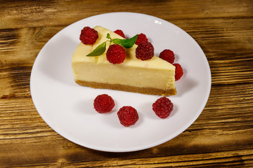 Piece of tasty New York cheesecake with raspberries in a white plate on wooden table