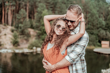 Fototapeta premium Thankful woman. Beaming curly woman smiling broadly feeling very thankful while having romantic date near rocks