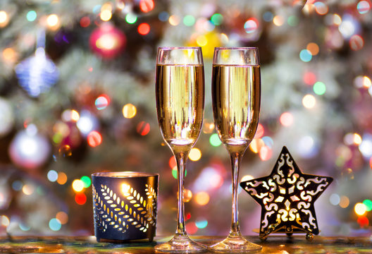 Christmas glasses with champagne on the background of the Christmas tree with toys decorated with colorful lights with star-shaped candlesticks