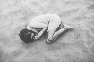 junge brünette Frau im Sand am Strand, zusammengekauert