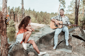 Fall in love. Beautiful curly woman wearing white sneakers falling in love while listening to her man playing the guitar