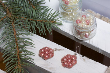 Blue spruce branches on a wooden box of boards, painted in white. Nearby there are earrings and there are jars with beads.