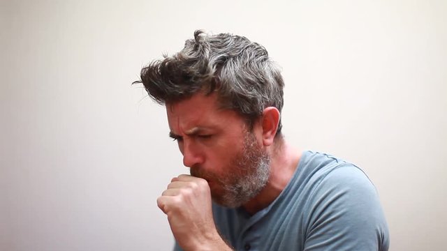 Handsome man coughing into his fist, isolated on a gray background