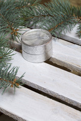 Blue spruce branches on a wooden box of boards, painted in white. Nearby is a silver gift box with a bow.