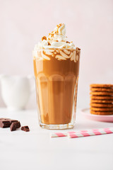 Chocolate ice coffee with whipped cream and cookies in a tall glass with pink straws on white marble table over rose background. High resolution image with copy space and selective focus.