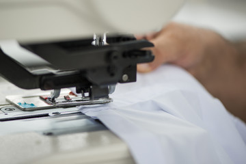 seamstress male on a sewing machine makes a shirt in the sewing workshop. the man on the machine sews the collar and cuffs