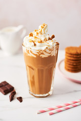 Chocolate ice coffee with whipped cream and cookies in a tall glass with pink straws on white marble table over rose background. High resolution image with copy space and selective focus.