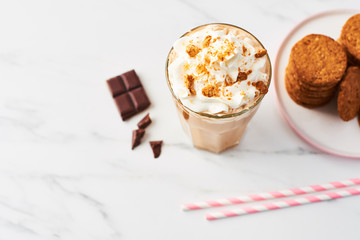 Chocolate ice coffee with whipped cream and cookies in a tall glass with pink straws on white marble table top. High resolution image with copy space and selective focus.