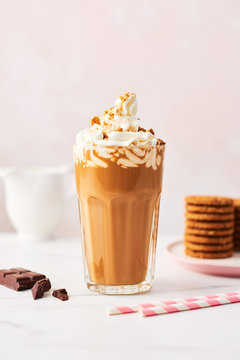 Chocolate ice coffee with whipped cream and cookies in a tall glass with pink straws on white marble table over rose background. High resolution image with copy space and selective focus.