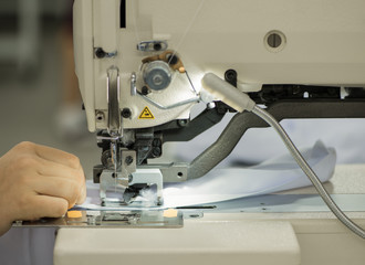 seamstress on a sewing machine makes a shirt in the sewing workshop. the woman on the machine sews the collar and cuffs