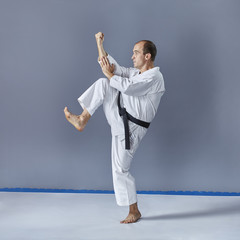On a gray background an athlete in white karategi and with a black belt trains formally karate exercises.