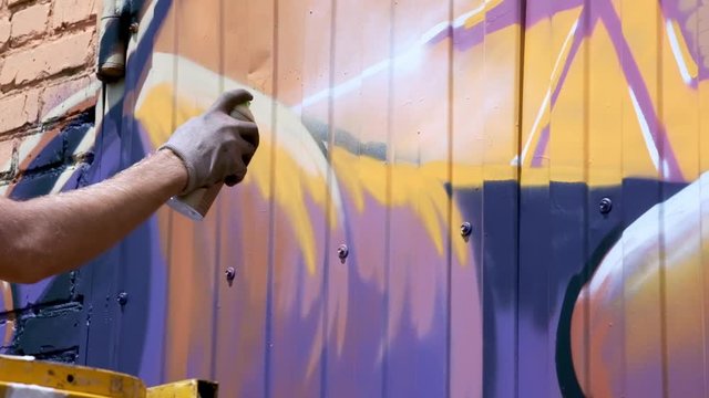 A young guy with a can of paint draws graffiti on the wall. One hand close-up. Slow motion