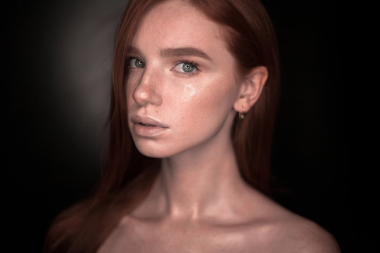 Serious redhead girl woman with healthy glow wet skin posing isolated over black wall background looking at camera.