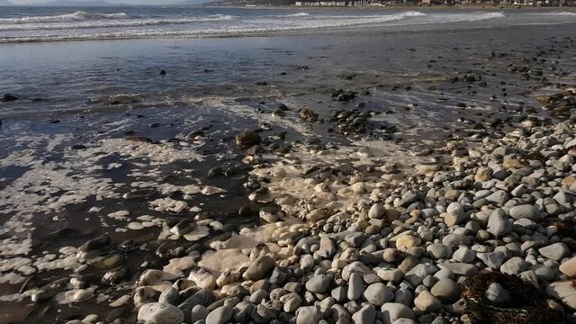 Waves lapping the shore with pebbles and sea foam.