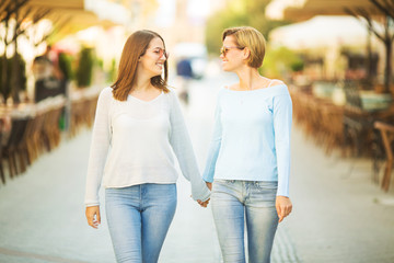 Two happy young woman holding hands while walking