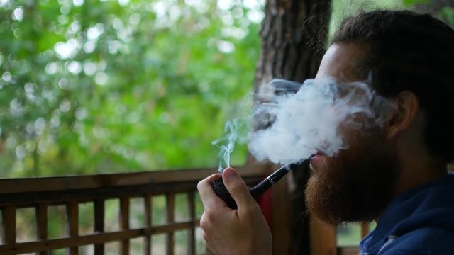 Close up of attractive man with beard smoking on the beach. Outside. Portrait
