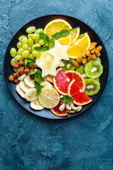 Healthy vegetarian bowl dish with fresh fruits and nuts. Plate with raw apple, orange, grapefruit, banana, kiwi, lemon, grape, almond, hazelnut and cashew nuts. Healthy balanced eating