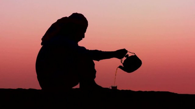 Loop of A Bedouin man pours tea in silhouette against the sunset. Loop 2 of 3.