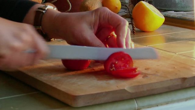 Loop of A woman chef slices fresh tomatoes on a wooden cutting board.