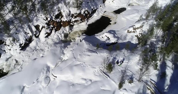 Lapland rapids, C4K aerial descending tilt view of a man taking pictures of kiutakongas rapid, in Oulanka national park, on a sunny, winter day, in Kuusamo, Pohjois-Pohjanmaa, Finland
