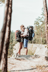 Hugs and hiking. Tender curly dark-haired woman with heavy backpack hugging her strong bearded man while hiking