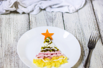 Christmas tree from a salad olivier in plate on a white wooden table. Top view with a copy space