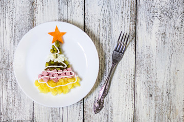 Christmas tree from a salad olivier in plate on a white wooden table. Top view with a copy space