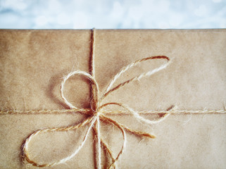 The gift is wrapped in craft paper and tied with a rough rope. A close up shows a bow made of rope....