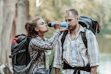Cold water. Curly appealing dark-haired woman with backpack drinking some cold water after hiking...