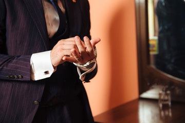 The rundown plan is a cropped frame of a stylish businessman marries today, put on a fashionable suit, wears a white shirt and stylish expensive leather watches, fastens cuff links on his sleeve.