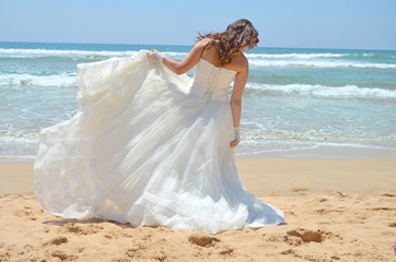 Fototapeta na wymiar Long-haired brunette bride straightens her dress standing on the sand, the beach on the Indian Ocean. Wedding and honeymoon in the tropics on the island of Sri Lanka