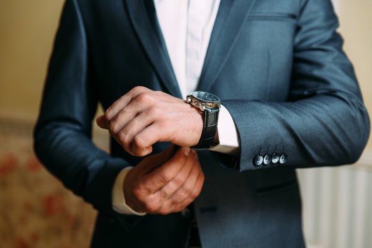 A close-up of a cropped frame of a man in an expensive classic costume looks at his watch. The businessman is in a hurry and looks at the time. A handsome man with a precious watch and a gold ring.