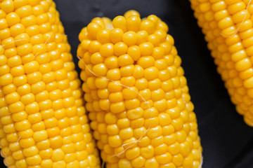 fresh boiled corn of golden color on a black plate top view