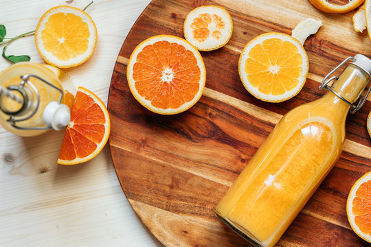 A Glass Bottle Of Fresh Juice Lies On A Dark Wooden Plate With Sliced Orange Slices Flatlay